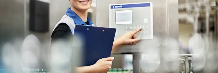 Das Foto zeigt eine junge Frau vor einem Display mit Klemmbrett in der Hand