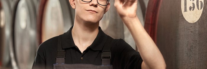 Das Foto zeigt einen jungen Mann der ein Glas mit einem Flüssigkeit vors Licht hält