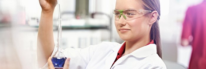 Das Foto zeigt eine junge Frau in weißem Kittel mit Kolben und Pipette in der Hand